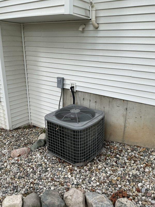 Conducted sales estimate for air conditioning system installation at residential property with existing outdoor condenser unit positioned on gravel bed against exterior wall with vinyl siding. Customer previously purchased furnace and requested mid-range AC system pricing, expressing intent to proceed with installation scheduled for later in the week. Documented existing HVAC equipment setup including electrical disconnect box, conduit connections, and foundation placement for proper system sizing and installation planning.