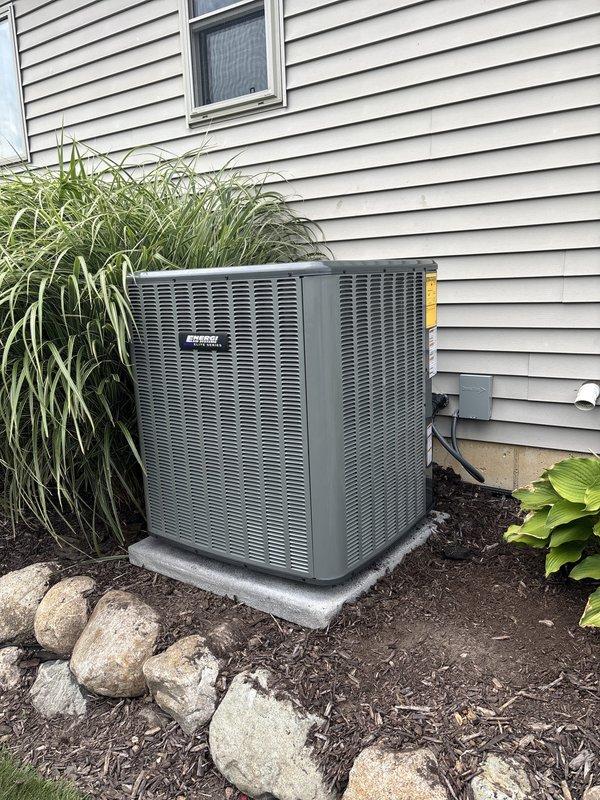 Completed full air conditioning system replacement including outdoor condensing unit and indoor air handler. Installed new Carrier equipment with proper refrigerant line connections, electrical conduit routing through exterior siding, and secure mounting on concrete pad. Unit positioned in landscaped side yard area with decorative rock placement maintained around base. Indoor installation included air handler integration with existing furnace system in basement utility area, new metallic ductwork with curved elbow transition, and proper sealing of all connections. Verified all electrical connections, tested system operation, and confirmed proper airflow throughout. Installation completed as same-day service per authorized work order.
