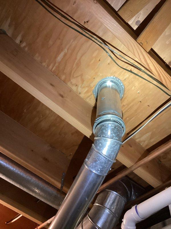Conducted on-site evaluation of existing 40-gallon conventional tank water heater for replacement estimate in 27-year-old residential property. Inspected current water heater installation in basement utility area, documenting existing venting system with metal ductwork extending through wooden floor joists, copper supply line connections with shutoff valve, and concrete base platform. Photographed installation configuration including vertical venting arrangement and plumbing connections to provide accurate replacement specifications for standard tank-type water heater unit.