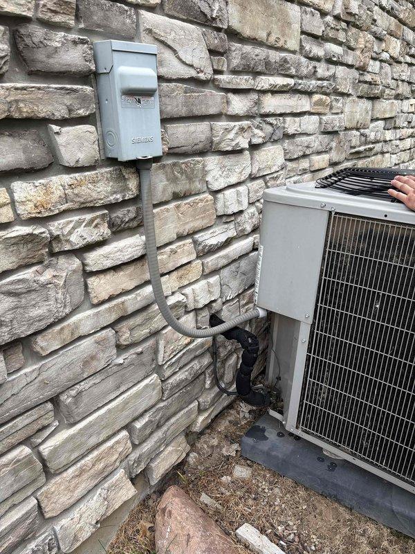 Responded to client request for assessment of unlevel air conditioning condenser unit. Upon arrival, performed visual inspection of 9-year-old Bryant residential AC system installed on concrete pad against exterior stone wall. Documented current installation conditions showing condenser unit settling unevenly on pad, with unit positioned on black rubber isolation pad surrounded by decorative river rock landscaping. Verified electrical disconnect box and conduit connections properly secured to wall. Photographed equipment positioning, pad condition, and surrounding grade to document extent of settling and provide basis for leveling estimate. Advised client that uneven condenser placement can lead to compressor damage, reduced efficiency, and premature system failure if not corrected. Provided detailed estimate for leveling service to restore proper equipment installation and prevent future mechanical issues.