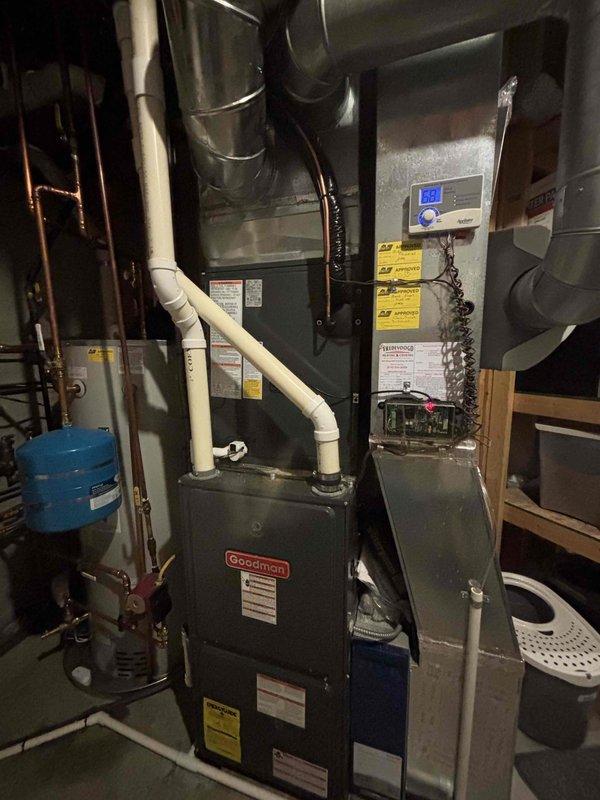 Completed full replacement of two residential air conditioning systems in a same-day installation. Removed existing HVAC equipment and installed new Goodman brand furnace units with integrated cooling systems in basement utility area. 

Installation included complete setup of air handler with proper electrical connections and digital control panel configuration. Ran and secured copper refrigerant lines along wall structures with appropriate insulation and support brackets. Installed blue expansion tank for system pressure regulation. Connected white PVC condensate drainage lines with proper slope and U-trap configuration to ensure efficient moisture removal from the system.

Integrated new equipment with existing ductwork infrastructure, including metallic supply and return ducts. Made all necessary electrical connections to control boards and verified proper voltage and amperage to digital display panels. Ensured all manufacturer warning labels and specification plates remained visibl