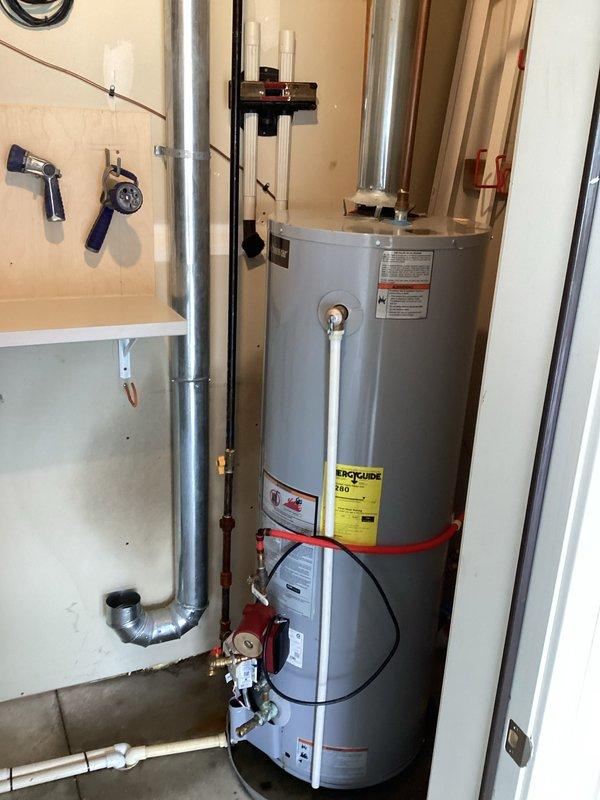 Responded to emergency water heater leak causing active flooding and drywall damage. Inspected 5-year-old Lochinvar water heater system and identified source of leak at base of unit. Documented extensive water damage to surrounding drywall and flooring from ongoing leak. Photographed complete installation including water heater, expansion tank, copper supply lines with red and blue foam insulation, PVC connections, and mounting configuration. Provided customer with replacement estimate as requested due to age of unit and severity of leak compromising structural integrity of utility room.