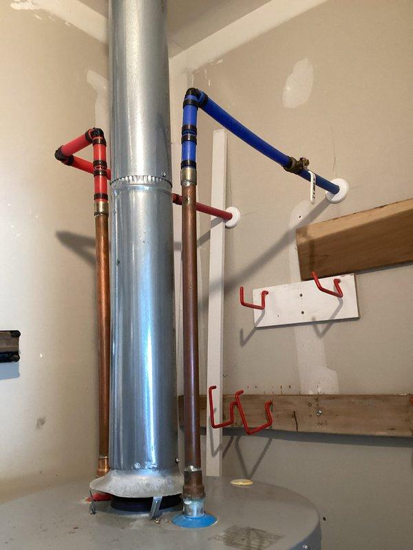 Responded to emergency water heater leak causing active flooding and drywall damage. Inspected 5-year-old Lochinvar water heater system and identified source of leak at base of unit. Documented extensive water damage to surrounding drywall and flooring from ongoing leak. Photographed complete installation including water heater, expansion tank, copper supply lines with red and blue foam insulation, PVC connections, and mounting configuration. Provided customer with replacement estimate as requested due to age of unit and severity of leak compromising structural integrity of utility room.