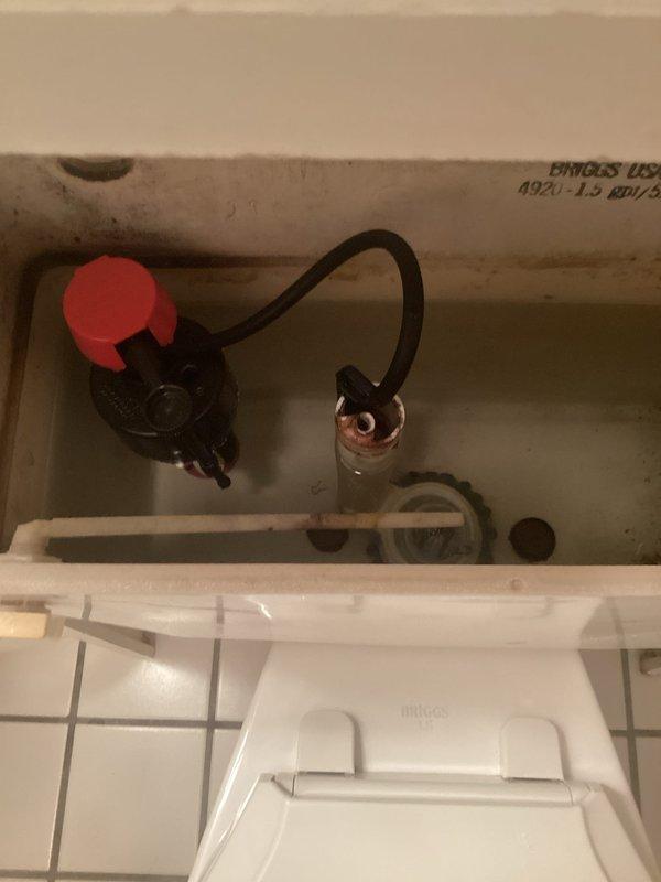 Responded to toilet issue in approximately 30-year-old residence. Inspected toilet tank interior and identified worn flush valve assembly with deteriorated red rubber flapper causing intermittent or incomplete flushing. Documented existing braided metal supply line connection, fill valve assembly, and mineral deposits consistent with age of fixture. Photographed tank components and water staining for service records.