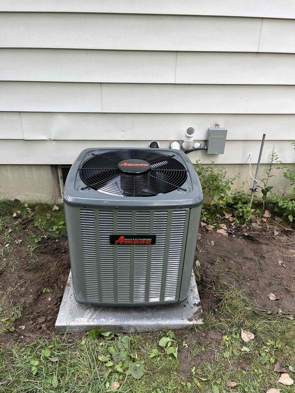 Completed full air conditioning system replacement with installation of new Amana outdoor condensing unit. Unit was properly positioned on concrete pad with appropriate clearances from structure. Refrigerant lines were installed and insulated, electrical disconnect box mounted to exterior wall, and all connections properly secured. System was charged with A2L refrigerant to manufacturer specifications with factory charge of 52 oz and total system charge of 52.4 oz documented on unit labeling. All service valves installed with protective caps, system tested and verified operational with proper airflow through top-mounted fan assembly.