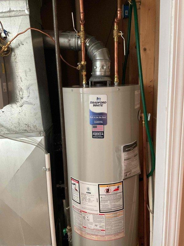 Completed installation of a 40-gallon natural draft, natural gas Bradford White water heater with short tank configuration (48 1/16" height) in residential utility space. Connected copper supply lines with brass fittings, installed temperature and pressure relief valve, and properly vented unit with metallic vent pipe extending from top of heater. Installation includes 6-year parts and 1-year labor warranty coverage.