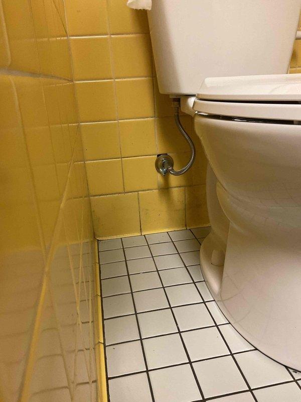 Completed toilet installation in bathroom with yellow tile walls and white mosaic floor tile. Unit properly secured, water supply line connected, and system tested for proper function and leaks. Installation verified operational with no issues detected.