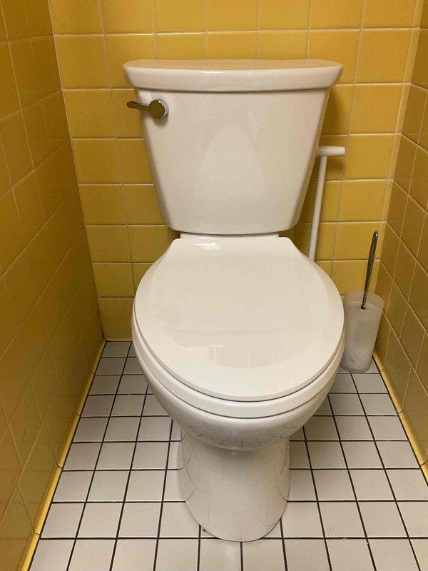 Completed toilet installation in bathroom with yellow tile walls and white mosaic floor tile. Unit properly secured, water supply line connected, and system tested for proper function and leaks. Installation verified operational with no issues detected.