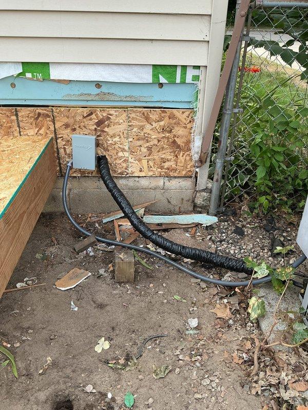 Completed quoted repair work on residential HVAC system requiring refrigerant service. Accessed exterior wall opening with OSB covering and installed electrical conduit routing from junction box to ground level. Serviced outdoor condensing unit, performing refrigerant work on the aging system positioned on concrete pad in backyard area. Work completed over 3-4 hour timeframe with additional technician return visit scheduled for refrigerant charging procedures.