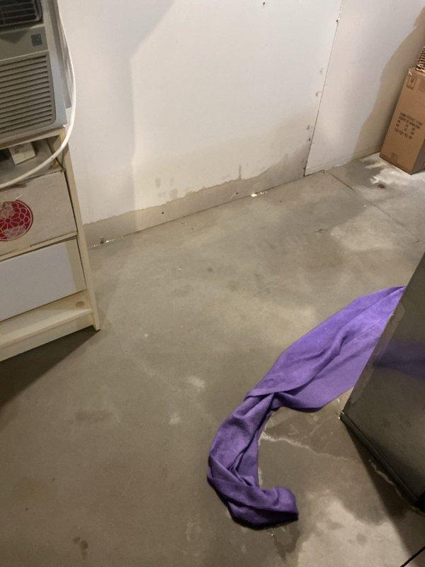 # Water Leak Service Call

Responded to water leak in basement utility area. Upon arrival, found active water intrusion affecting concrete floor with visible moisture and standing water in corner near HVAC equipment. Identified source of leak originating from plumbing system along wall where multiple PVC pipes converge. 

Deployed absorbent materials to contain spreading water and protect nearby stored items and cardboard boxes. Assessed extent of water damage to unfinished basement space, noting moisture penetration on concrete floor and potential impact to wall materials in various stages of construction. Inspected white window air conditioning unit positioned in affected area to ensure no water damage to electrical components.

Evaluated plumbing configuration and pipe connections at corner junction where leak was most prominent. Documented conditions of surrounding construction materials including exposed framing, drywall panels, and wall openings. Provided recommendations for wate