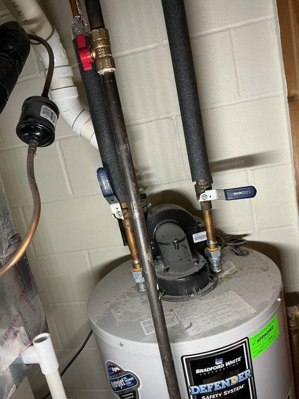 Responded to service call for leaking water heater. Upon arrival, inspected 12-year-old Bradford White Defender Safety System water heater installed in basement utility area. Conducted thorough visual examination of unit, including all pipe connections, valves, and fittings at top of tank. Inspected copper supply lines with foam insulation, ball valves with blue and red handles, and circulator pump assembly. Documented existing installation configuration showing proper mounting to concrete block wall with secure pipe clamps and brackets. Photographed water heater condition, piping layout, valve positions, and overall system setup for customer records and assessment purposes.
