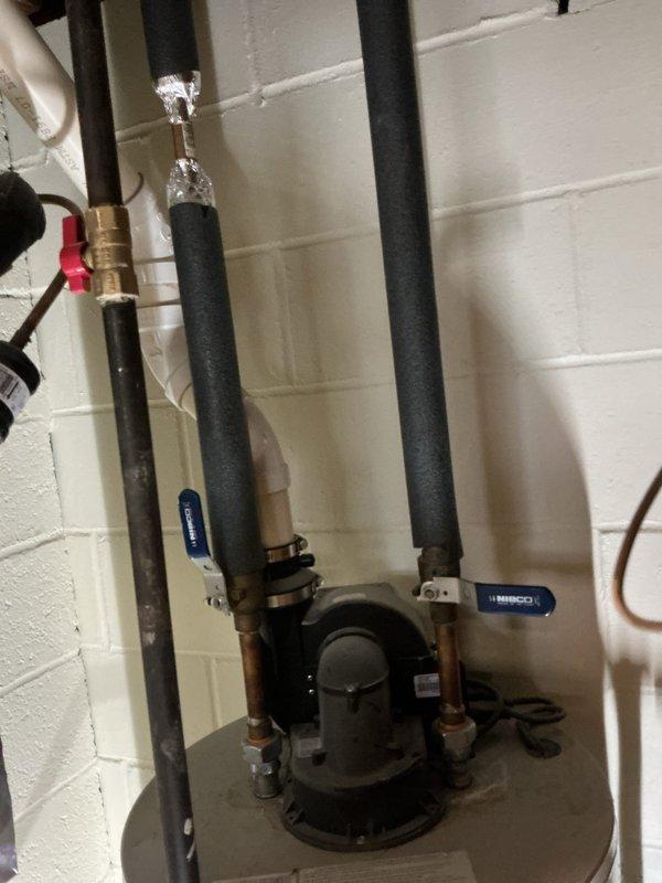 Responded to service call for leaking water heater. Upon arrival, inspected 12-year-old Bradford White Defender Safety System water heater installed in basement utility area. Conducted thorough visual examination of unit, including all pipe connections, valves, and fittings at top of tank. Inspected copper supply lines with foam insulation, ball valves with blue and red handles, and circulator pump assembly. Documented existing installation configuration showing proper mounting to concrete block wall with secure pipe clamps and brackets. Photographed water heater condition, piping layout, valve positions, and overall system setup for customer records and assessment purposes.