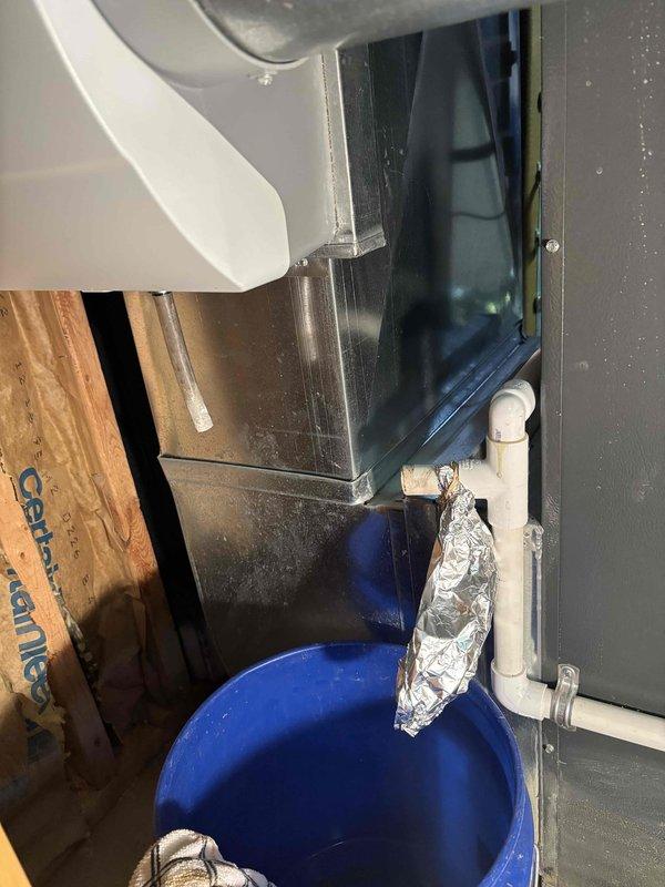 Responded to air conditioner drain leak on a twelve-year-old EnergiAir system. Upon arrival, found condensate drainage system experiencing water discharge issues while unit maintained normal cooling operation. Temporarily placed collection bucket beneath affected drain line to contain water until proper repair could be completed. System remains functional with cooling capacity unaffected by drainage concern.
