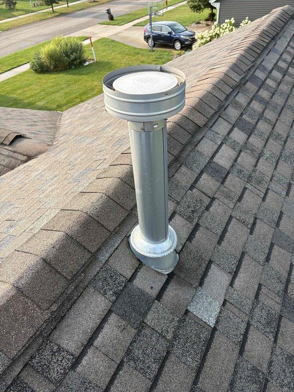 Responded to water heater alarm complaint with reported source above unit. Upon inspection, located water heater exhaust vent on rooftop with severe ice and frost accumulation on ductwork and flue pipe. Ice buildup on metal vent components was causing blockage and triggering alarm system. Documented conditions showing extensive frost coating on cylindrical duct collar, flange connections, and vertical flue stack penetrating roof surface. Identified restricted airflow due to frozen condensation accumulation as root cause of alarm activation. Recommended immediate ice removal from exhaust components and evaluation of venting system for proper draft and condensation management to prevent future freezing issues.