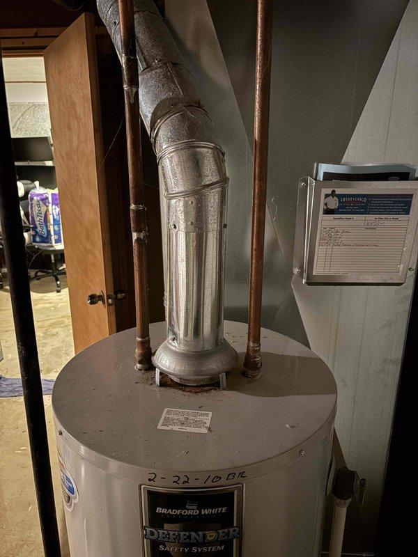 Responded to emergency call for water heater leaking in basement of 50-year-old residential property. Upon arrival, inspected Bradford White Defender Safety System water heater unit dated 2-22-10. Conducted thorough visual assessment of tank, connections, and surrounding plumbing infrastructure including copper supply lines and galvanized vent piping. Documented condition of unit and all associated components with photographic evidence. Evaluated integrity of flue assembly, water connections, and potential leak sources on aging tank system. Provided customer with findings and recommended course of action for resolution.
