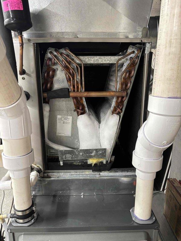 Responded to service call for outdoor air conditioning unit damaged by fallen tree. Upon arrival, confirmed system was still operational and providing cooling despite physical damage to exterior unit. Conducted interior inspection of HVAC system and documented condition of evaporator coil assembly. Found A-frame evaporator coil showing significant age-related oxidation and discoloration on copper tubing, with condensate present in drain pan indicating active operation. All interior components including coil assembly, insulation, and drainage lines were photographed for documentation purposes. System confirmed functional at time of inspection.