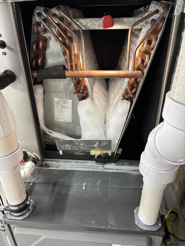 Responded to service call for outdoor air conditioning unit damaged by fallen tree. Upon arrival, confirmed system was still operational and providing cooling despite physical damage to exterior unit. Conducted interior inspection of HVAC system and documented condition of evaporator coil assembly. Found A-frame evaporator coil showing significant age-related oxidation and discoloration on copper tubing, with condensate present in drain pan indicating active operation. All interior components including coil assembly, insulation, and drainage lines were photographed for documentation purposes. System confirmed functional at time of inspection.