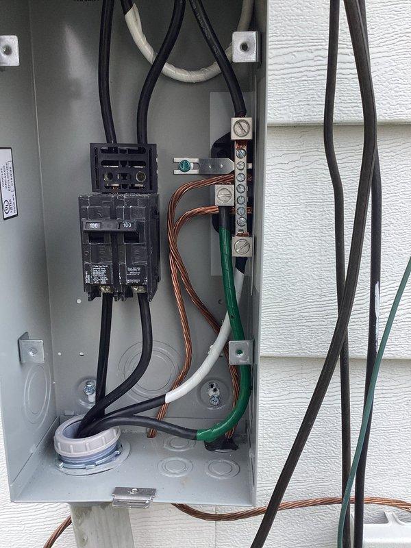 Responded to inspector correction request for electrical and plumbing system evaluation. Documented outdoor electrical panel installation showing two circuit breakers, proper grounding connections with copper and multi-colored conductors terminated to neutral bar, and multiple cable entries through top knockouts. Inspected and photographed copper water supply line with shutoff valve showing signs of corrosion and mineral buildup at lower connection point near pump unit, with proper pipe mounting and grounding wire installation throughout system.