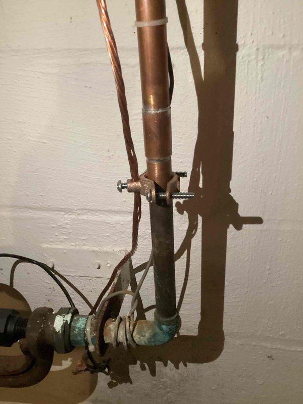 Responded to inspector correction request for electrical and plumbing system evaluation. Documented outdoor electrical panel installation showing two circuit breakers, proper grounding connections with copper and multi-colored conductors terminated to neutral bar, and multiple cable entries through top knockouts. Inspected and photographed copper water supply line with shutoff valve showing signs of corrosion and mineral buildup at lower connection point near pump unit, with proper pipe mounting and grounding wire installation throughout system.