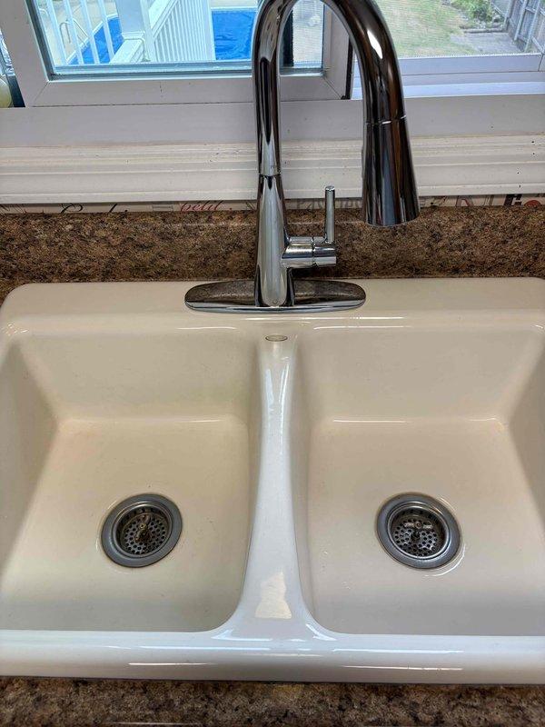 Replaced malfunctioning kitchen faucet with customer-supplied chrome pull-down unit on double-basin white sink. Removed existing faucet that was difficult to operate, installed new faucet assembly with proper mounting and connections, verified water flow and drainage system functionality, and confirmed no leaks at supply lines or drain connections.