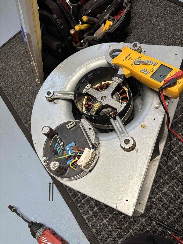 Responded to no cooling call for bedroom unit. Upon arrival, found blower motor inoperative while other units in home functioning normally. Disassembled blower assembly and performed electrical diagnostics using multimeter to test motor windings and connections. Tested amperage draw with clamp meter and inspected internal copper windings and capacitor connections. Motor exhibited failed windings consistent with age-related failure on 2017 equipment. Documented findings with photos showing disassembled motor assembly with exposed stator coils and electrical testing in progress. Provided customer with repair options for failed blower motor replacement.