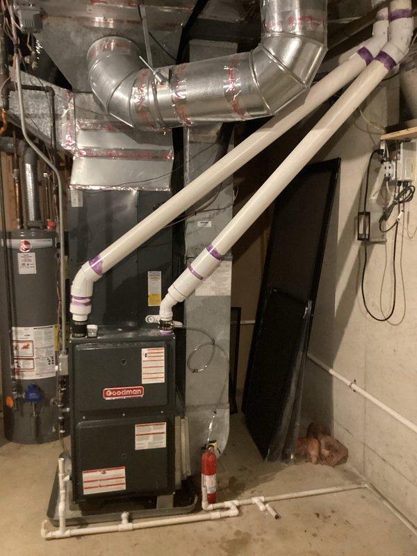 Completed installation of new PVC venting and condensate drain system for Goodman furnace. Installed white PVC exhaust pipes with proper securing bands and purple couplings, running from furnace unit to exterior termination point. Replaced condensate drain lines with clear tubing, properly secured with metal clips to air handler panel. Sealed all ductwork connections with aluminum foil tape at elbow joints. Verified proper pitch on drain lines and tested system operation to ensure adequate venting and drainage function.