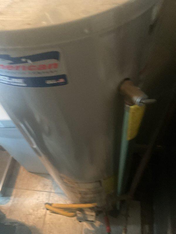 Responded to service call for water heater leaking at bottom. Upon inspection, found existing American brand water heater with visible deterioration and active leak at base of unit. Documented current condition showing aged equipment with compromised tank integrity. Provided estimate for complete water heater replacement, including removal of failed unit and installation of new equipment with appropriate connections and code-compliant installation.