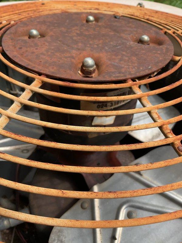 Responded to no-cooling call for 25-year-old residential outdoor HVAC unit that failed to operate. Upon arrival, found condenser unit completely inoperative with extensive rust and corrosion throughout the fan guard assembly and top plate. Inspected heavily weathered condenser fan motor assembly, protective cage, and mounting components showing significant oxidation from prolonged environmental exposure. Unit's advanced age and deteriorated condition indicated end of serviceable life, requiring full system replacement to restore cooling functionality.
