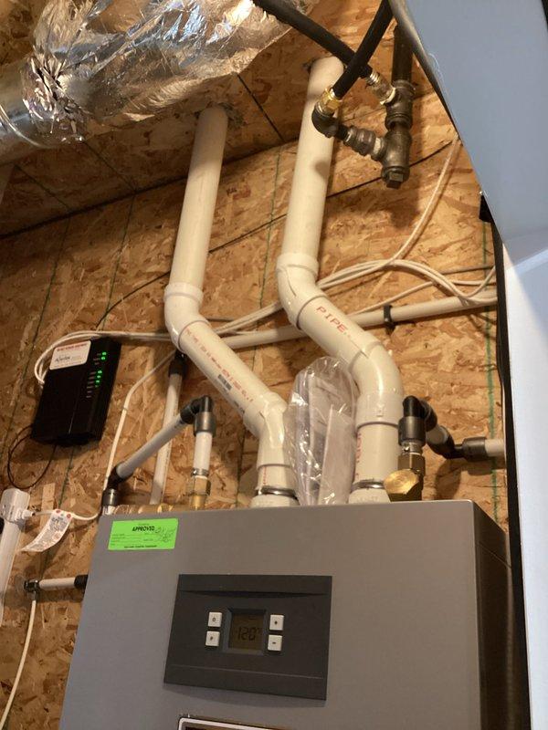 Responded to service call for inconsistent hot water production from instantaneous water heater. Upon inspection, found Rinnai RTG-K-199N1 tankless water heater with 199,000 BTU/Hr capacity installed in attic space. Evaluated complete installation including PVC venting system, gas supply lines with brass valves and fittings, water supply connections, and electrical components. Documented existing plumbing configuration showing properly routed white PVC vent piping with multiple elbows and T-joints, copper and flexible metal tubing connections, and digital control panel with LED indicators. Verified manufacturer specifications and unit serial number for service records. Photographed complete installation layout including Category IV venting system, control module with green indicator lights, and flexible metal ducting. System assessment completed to diagnose intermittent hot water issue.
