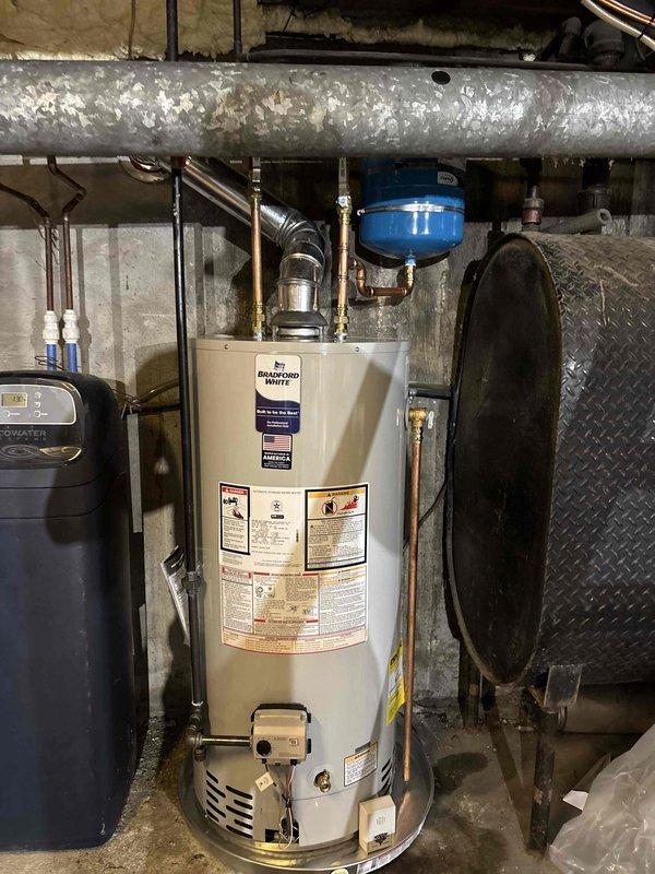 Successfully installed a new Bradford White automatic storage water heater in the basement utility area. Removed the existing water heater unit and installed the replacement, connecting all necessary copper supply lines, gas connections, and venting systems. Installed expansion tank and verified all connections were properly secured with appropriate brass fittings. Ensured compliance with manufacturer specifications including BTU ratings, pressure requirements, and natural gas specifications as indicated on unit labeling. Tested all connections for leaks, verified proper ventilation, and confirmed hot water delivery throughout the system. All safety labels and operational instructions remain visible and intact on the installed unit.