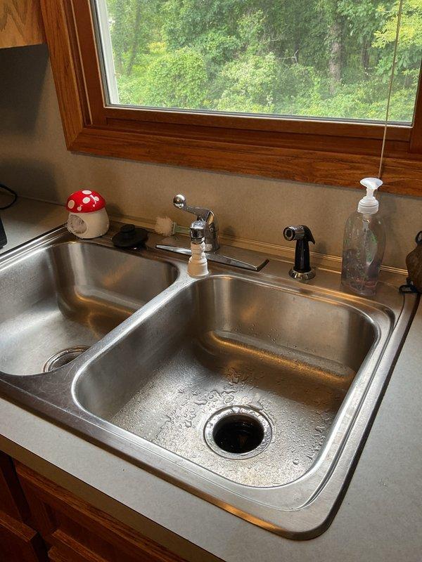 Responded to service call for leaky kitchen faucet and bathtub faucet with temperature control issues in a thirty-year-old residence. Inspected kitchen double-basin sink with chrome center-mount faucet and side spray attachment, identifying source of leak and performing necessary repairs to restore proper function. Addressed bathtub single-handle wall-mount faucet assembly where spout showed improper installation with visible gap between fixture and wall; repositioned and secured spout to eliminate leak potential and adjusted temperature control mechanism to ensure consistent water temperature regulation. Documented conditions with photographs for service records.