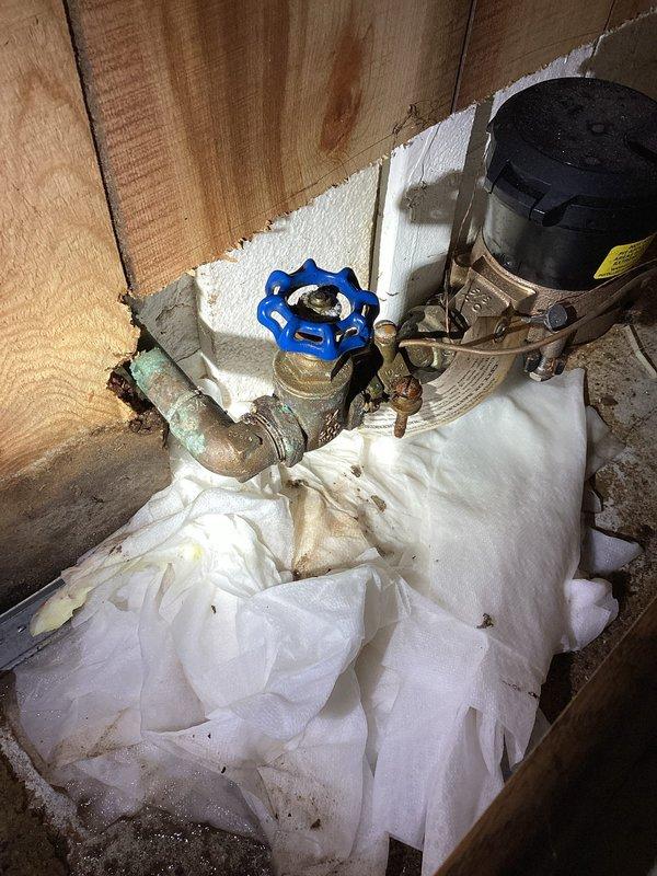 # Plumbing Leak Repair - Basement Utility Area

Responded to plumbing leak in basement utility area affecting concrete floor and surrounding space. Upon inspection, identified active leak originating from corroded metal piping system connected to pump assembly. The existing copper and galvanized piping showed extensive deterioration with visible patina, rust, and compromised integrity at connection points near blue-handled shutoff valve.

Shut down water supply to affected area and assessed extent of water damage. Concrete floor exhibited significant water staining and saturation across multiple zones, indicating leak had been present for extended period. Removed saturated materials and debris from work area to access plumbing components.

Repaired compromised pipe sections and connections at pump assembly. Tightened loose fittings and replaced deteriorated components to restore system integrity. Applied appropriate sealant materials where necessary to prevent future seepage. Tested sy