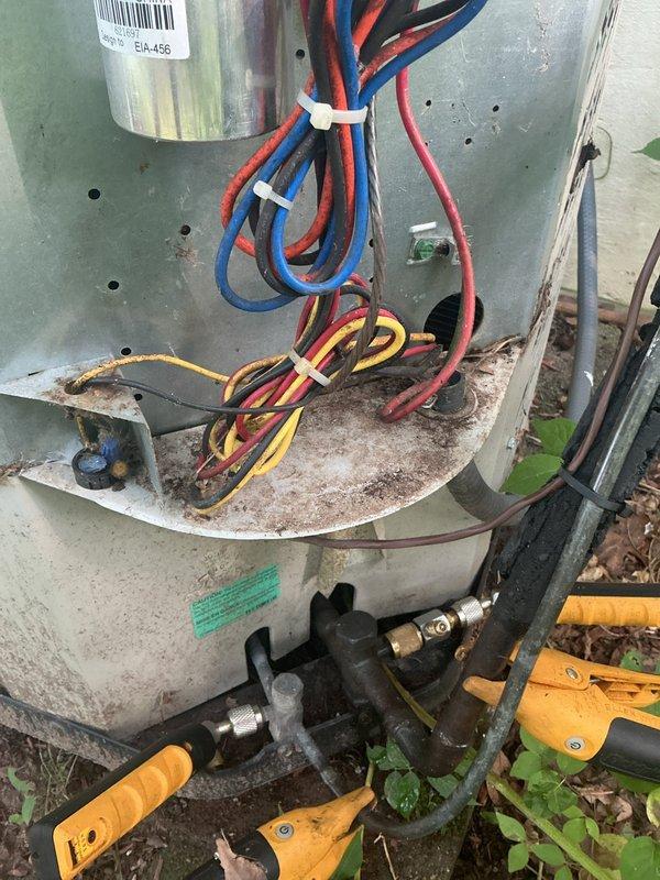 Completed annual cooling maintenance on 11-year-old AC unit. Removed significant accumulation of leaves, twigs, and organic debris from interior cabinet that had collected on components and could have restricted airflow or caused operational issues. Inspected electrical connections, wiring bundles, and zip tie securements—all found in acceptable condition. Checked refrigerant lines, service valves, and brass fittings for proper operation. Noted weathering and rust staining on exterior base pan consistent with outdoor installation and age of equipment, but no structural concerns affecting system performance. Unit operational and ready for cooling season.