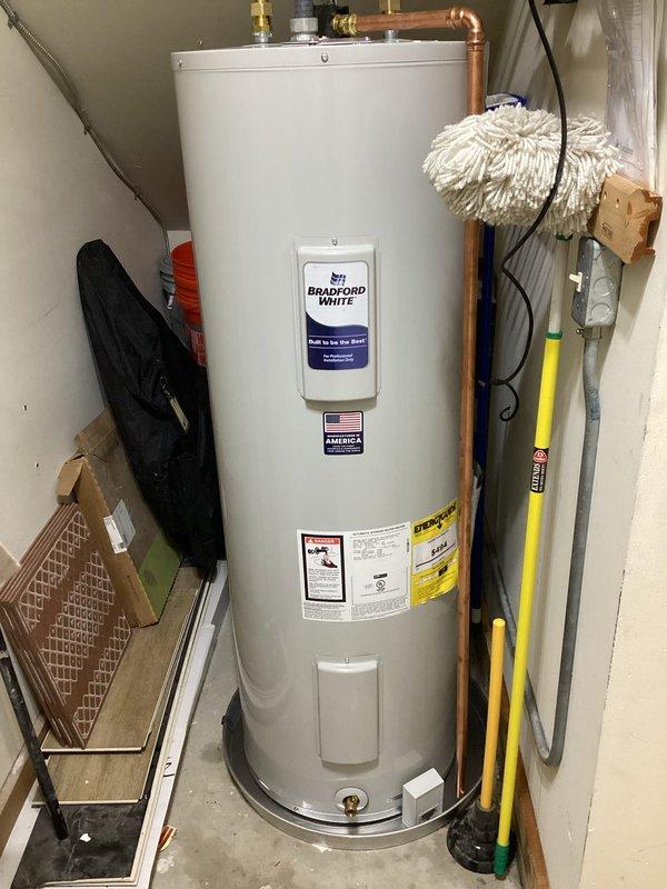Completed installation of a 50-gallon electric tall Bradford White water heater in utility closet. Connected copper supply lines with brass fittings and valves, secured electrical conduit to wall with cable ties, and verified all plumbing connections for proper operation. Unit installed per manufacturer specifications with all required safety labels visible and accessible.
