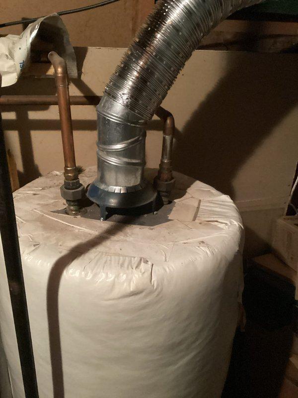Completed water heater estimate for residential property. Assessed existing water heater unit in basement utility area, noting standard residential configuration with copper supply lines, metallic flue adapter, and flexible aluminum exhaust vent ducting. Observed insulation blanket installed on unit for energy efficiency, with visible floor staining around base indicating potential previous moisture concerns. Documented equipment condition and installation specifications through photographic records to provide comprehensive replacement estimate for homeowner consideration.