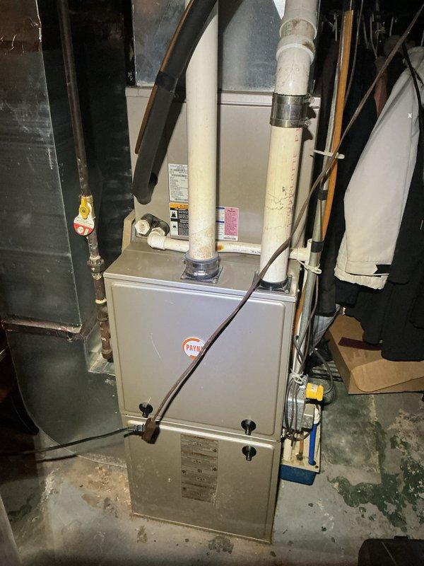 Completed annual cooling maintenance on a 13-year-old Payne air conditioning system. Performed comprehensive tune-up including inspection of outdoor condenser unit and indoor furnace components. Outdoor unit showed age-appropriate wear with surface rust and weathering on cabinet panels; confirmed proper mounting on concrete pad and verified electrical connections at disconnect box. Inspected indoor HVAC system, noting PVC exhaust pipe with previous duct tape repairs on joints. Documented system condition through photographs for maintenance records.