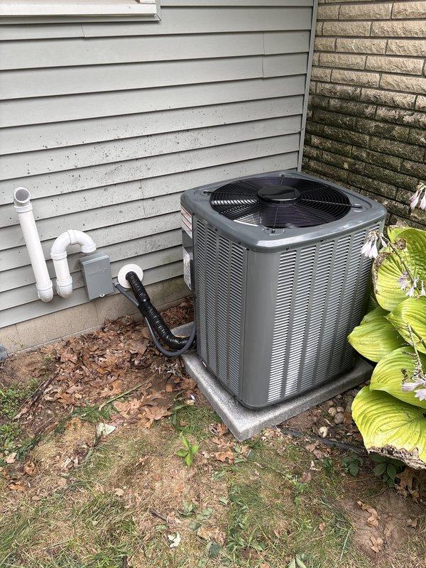 Complete HVAC system replacement performed, including installation of new outdoor condensing unit and indoor furnace. Outdoor unit positioned on existing concrete pad against exterior wall with proper clearances maintained, refrigerant lines connected, and condensate drainage installed using black flexible hose. Indoor furnace installed in basement utility area with new white PVC vent piping routed vertically, yellow gas line connected per code requirements, and silver metal ductwork integrated with existing distribution system. All electrical connections completed, system charged with refrigerant, and full operational testing performed to verify proper heating and cooling function.