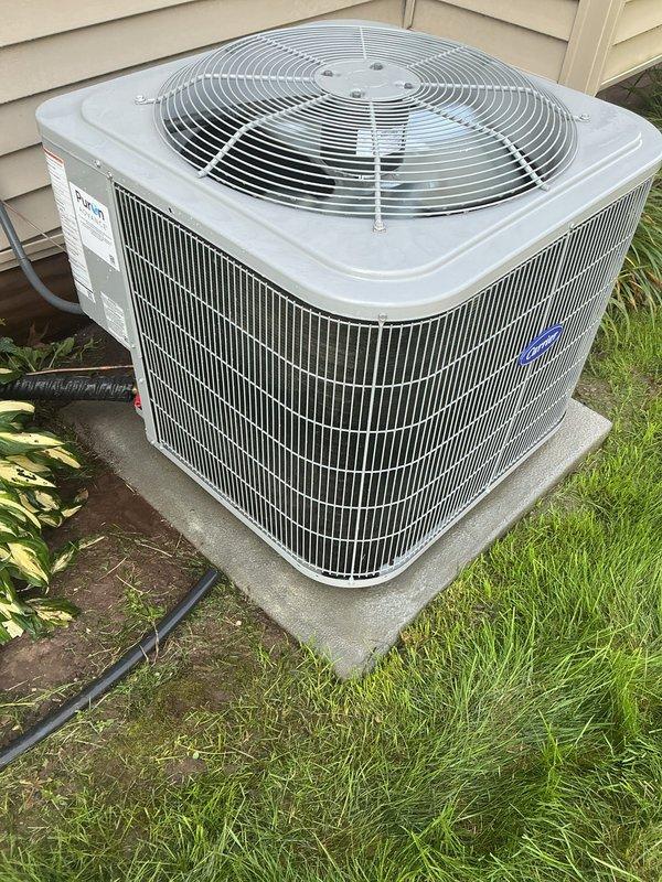 # Annual Cooling Maintenance - Carrier Condensing Unit

Completed comprehensive annual cooling maintenance on a 2018 Carrier outdoor condensing unit, model WT 03-2031. Performed visual inspection of the cylindrical condenser unit with vertical fin coil configuration, confirming proper installation on concrete pad with adequate clearance. Verified manufacturer labeling and unit identification information intact and legible.

Inspected condenser coil fins for damage, debris accumulation, and proper airflow clearance. Examined top-mounted fan guard assembly with radial wire spoke configuration for structural integrity. Checked condensate drainage line routing and confirmed proper discharge away from unit foundation. Evaluated electrical conduit and wiring connections for secure attachment and code compliance.

Assessed unit housing and cabinet condition, noting clean exterior surfaces with no visible corrosion, rust, or deterioration on metal components. Verified protective grilles and fa