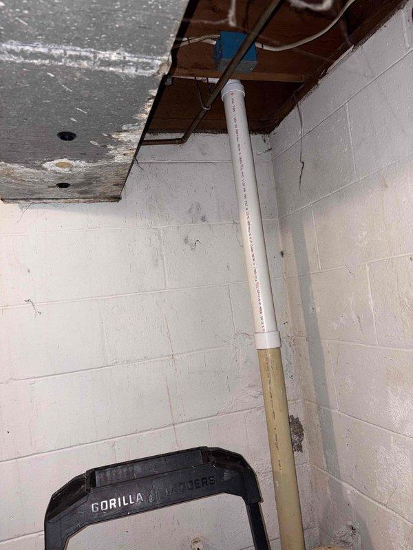 Completed kitchen drain rebuild involving replacement of deteriorated PVC drain piping in crawlspace area beneath kitchen. Installed new white PVC drain line with 90-degree elbow fittings to restore proper drainage flow, working around existing copper water supply lines and aged floor joists. Vertical drain stack connection completed where pipe transitions through floor structure to tie into existing plumbing system.