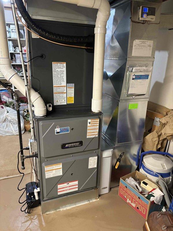 Complete residential air conditioning system replacement performed. Removed existing outdoor condensing unit and indoor air handler equipment. Installed new outdoor AC condenser on existing concrete pad with proper leveling and positioning against building exterior. Secured refrigerant line sets and electrical conduit from exterior wall to new condenser unit. Utilized existing PVC condensate drain lines for proper drainage. Indoor installation included new air handler unit positioned in basement utility area with integration to existing ductwork system. Connected all electrical components, refrigerant lines, and condensate drainage. Verified proper thermostat wiring and digital display functionality. Pressure tested refrigerant lines for leaks, evacuated system, and charged to manufacturer specifications. Performed system startup procedures and verified proper operation of both heating and cooling functions. Confirmed adequate airflow through supply ductwork and proper temperature diff