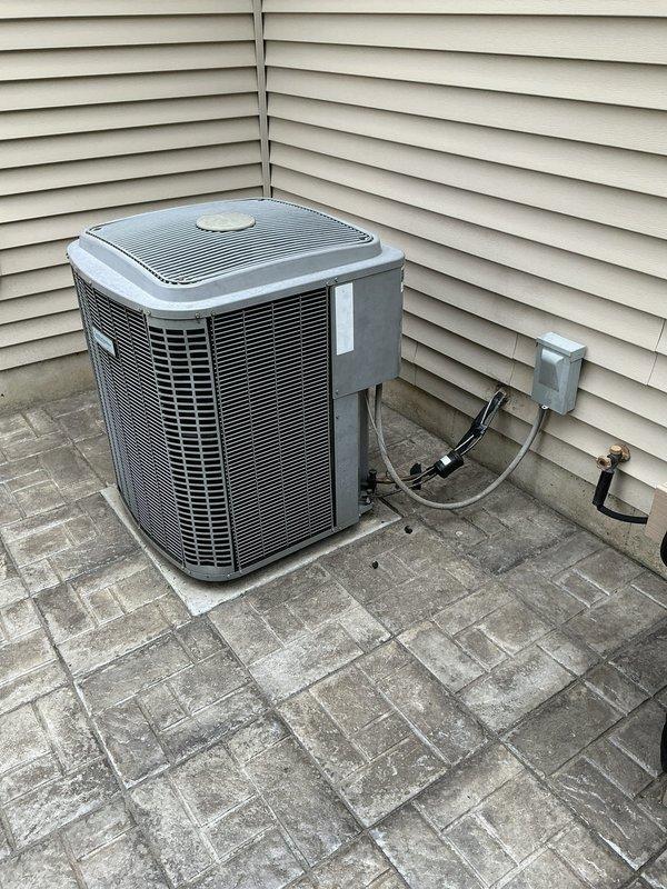 Completed on-site evaluation for full HVAC system replacement including furnace and air conditioning unit. Assessed existing outdoor condensing unit located at exterior corner of building, noting current refrigerant line routing, electrical disconnect configuration, and condition of installation pad and surrounding pavers. Inspected interior mechanical room and existing ductwork system, documenting galvanized steel trunk line assembly, flexible duct connections, and current equipment layout. Photographed both exterior AC unit and interior furnace/ductwork configuration to provide comprehensive documentation for equipment sizing and replacement proposal.