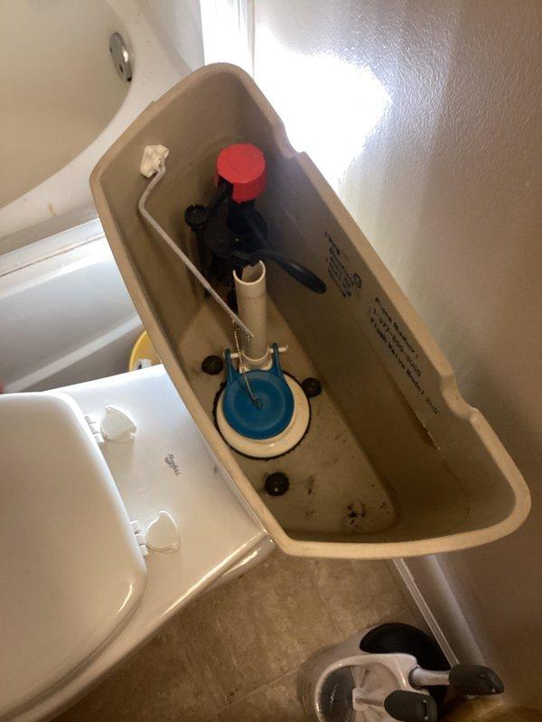 Responded to no-water issue affecting toilet in 21-year-old residence. Upon inspection, found fill valve assembly malfunctioning and preventing water from entering tank. Removed toilet tank lid and diagnosed faulty fill valve mechanism that was not responding to shutoff valve adjustments, explaining why issue persisted for several months. Documented existing tank components including blue flapper valve, overflow tube, and flush lever assembly with red float mechanism. Photographed internal tank condition showing standard residential flush system with visible wear and minor water staining consistent with age of fixture.