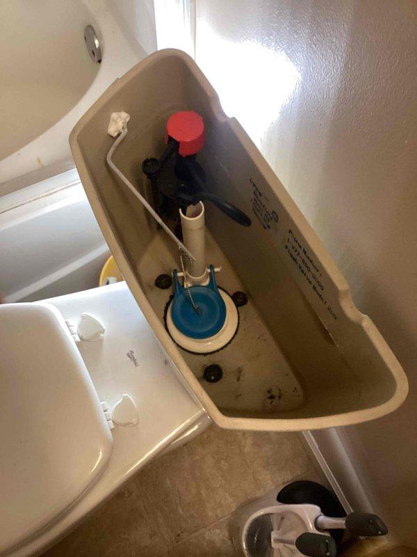 Responded to no-water issue affecting toilet in 21-year-old residence. Upon inspection, found fill valve assembly malfunctioning and preventing water from entering tank. Removed toilet tank lid and diagnosed faulty fill valve mechanism that was not responding to shutoff valve adjustments, explaining why issue persisted for several months. Documented existing tank components including blue flapper valve, overflow tube, and flush lever assembly with red float mechanism. Photographed internal tank condition showing standard residential flush system with visible wear and minor water staining consistent with age of fixture.