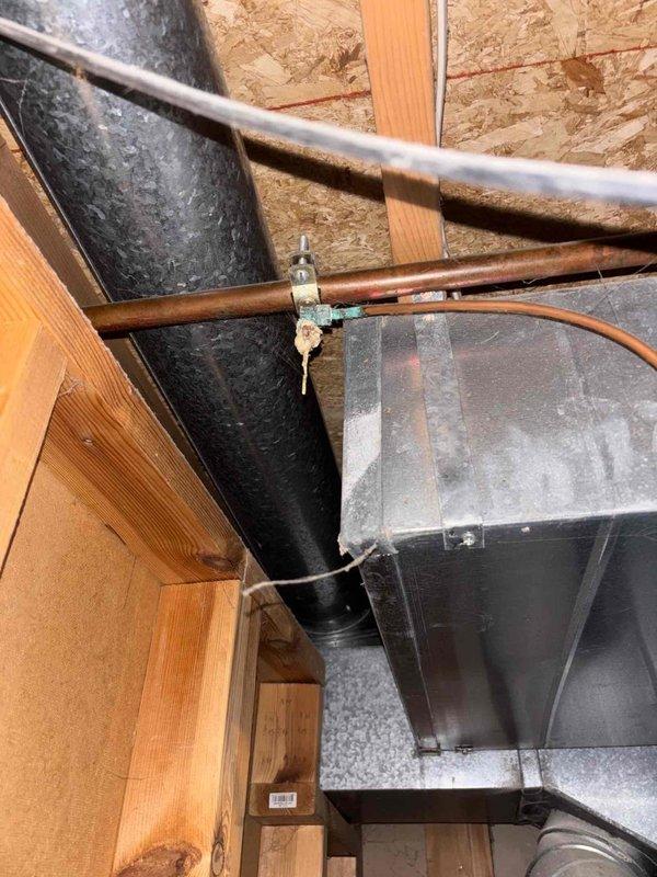 Responded to emergency plumbing leak in basement where burst pipe was actively leaking in multiple locations onto carpeted flooring. Primary leak source identified at water filter canister assembly with compromised brass elbow fitting connecting aged copper supply line to newer PEX piping. Shut off water supply to stop active flooding, assessed extent of damage to affected areas, and documented corroded copper pipe connections and deteriorated brass fittings requiring replacement. Photographed plumbing assembly showing transition point between old copper and modern PEX materials, along with HVAC components and structural elements in vicinity of leak. Provided immediate leak mitigation to prevent further water damage to basement carpet and surrounding areas.