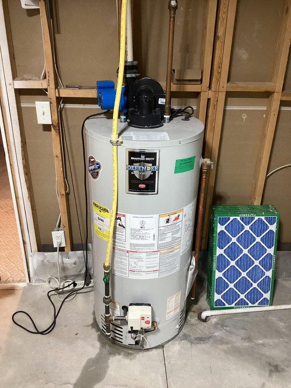 Responded to water heater service call and performed comprehensive inspection of Bradford White Defender series unit in residential utility room. Documented existing installation including gas line connections, electrical components, and plumbing configuration with copper piping and shutoff valves. Unit appeared operational with proper venting and all safety labels intact at time of inspection.