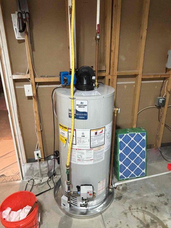 Responded to water heater service call and performed comprehensive inspection of Bradford White Defender series unit in residential utility room. Documented existing installation including gas line connections, electrical components, and plumbing configuration with copper piping and shutoff valves. Unit appeared operational with proper venting and all safety labels intact at time of inspection.