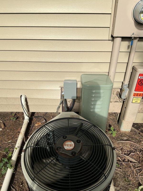 # Cooling Performance Issue - 29-Year-Old Payne System

Responded to service call for air conditioning unit not cooling adequately. Upon arrival, inspected 29-year-old Payne condensing unit located on exterior of residence. Performed visual assessment of outdoor unit, electrical disconnect box, and associated wiring.

Accessed electrical panel housing and inspected internal components including capacitor and contactor assembly. Noted weathering and outdoor exposure on electrical components with visible dirt accumulation and staining on metal surfaces. Examined capacitor connections with multiple wire terminations (yellow, black, red, green, and blue leads) and contactor relay for proper operation.

Documented equipment condition with photographs showing unit placement on mulch bed, electrical disconnect installation, conduit routing, and internal electrical component configuration. System evaluation completed to determine cause of reduced cooling performance and identify necessary repa
