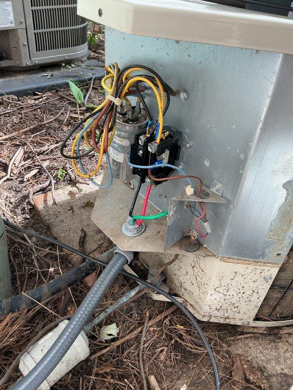 # Cooling Performance Issue - 29-Year-Old Payne System

Responded to service call for air conditioning unit not cooling adequately. Upon arrival, inspected 29-year-old Payne condensing unit located on exterior of residence. Performed visual assessment of outdoor unit, electrical disconnect box, and associated wiring.

Accessed electrical panel housing and inspected internal components including capacitor and contactor assembly. Noted weathering and outdoor exposure on electrical components with visible dirt accumulation and staining on metal surfaces. Examined capacitor connections with multiple wire terminations (yellow, black, red, green, and blue leads) and contactor relay for proper operation.

Documented equipment condition with photographs showing unit placement on mulch bed, electrical disconnect installation, conduit routing, and internal electrical component configuration. System evaluation completed to determine cause of reduced cooling performance and identify necessary repa