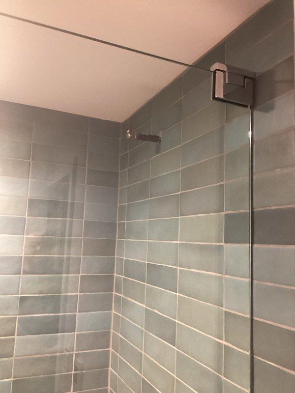 Completed plumbing project estimate for bathroom renovation requiring toilet and shower fixture installations. Assessment conducted on two bathroom areas: one small bathroom with existing vanity and prepared workspace showing active construction in progress, and one modern shower enclosure featuring gray-green tile work with chrome fixtures and glass door assembly already installed. Evaluated scope of work for installing new toilets and completing shower fixture connections in accordance with current plumbing codes and specifications.