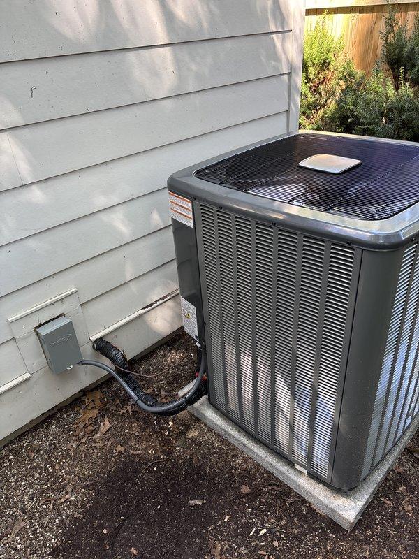 Completed full HVAC system replacement including outdoor condensing unit and indoor air handler components. Removed existing equipment and installed new dark gray condenser unit on existing concrete pad with proper clearances for airflow and serviceability. Mounted electrical disconnect box on exterior wall with conduit routing to unit. Inside utility area, installed furnace system with integrated cooling coil, completed refrigerant line connections using copper piping, and installed PVC condensate drainage with proper pitch and routing to ceiling. Verified all electrical connections at junction boxes, tested system operation across heating and cooling modes, and confirmed proper airflow, refrigerant charge, and temperature differential. System operational and ready for service.